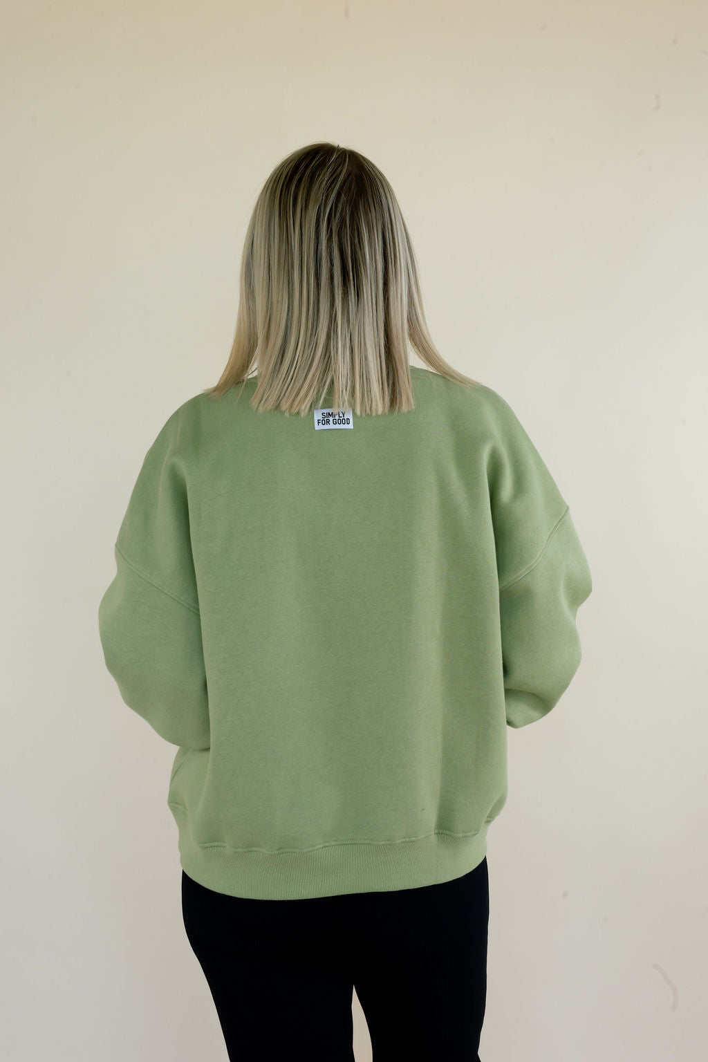 Back view of sage green Simply For Good sweatshirt featuring relaxed fit, ribbed hem, and small Simply For Good neck label