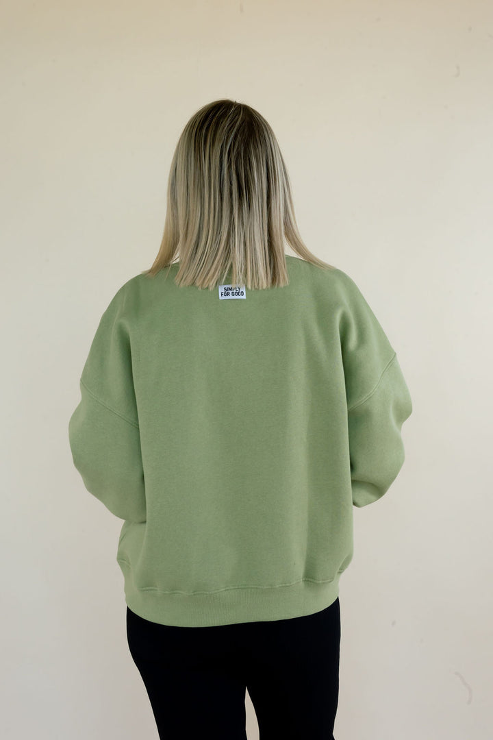 Back view of sage green Simply For Good sweatshirt featuring relaxed fit, ribbed hem, and small Simply For Good neck label