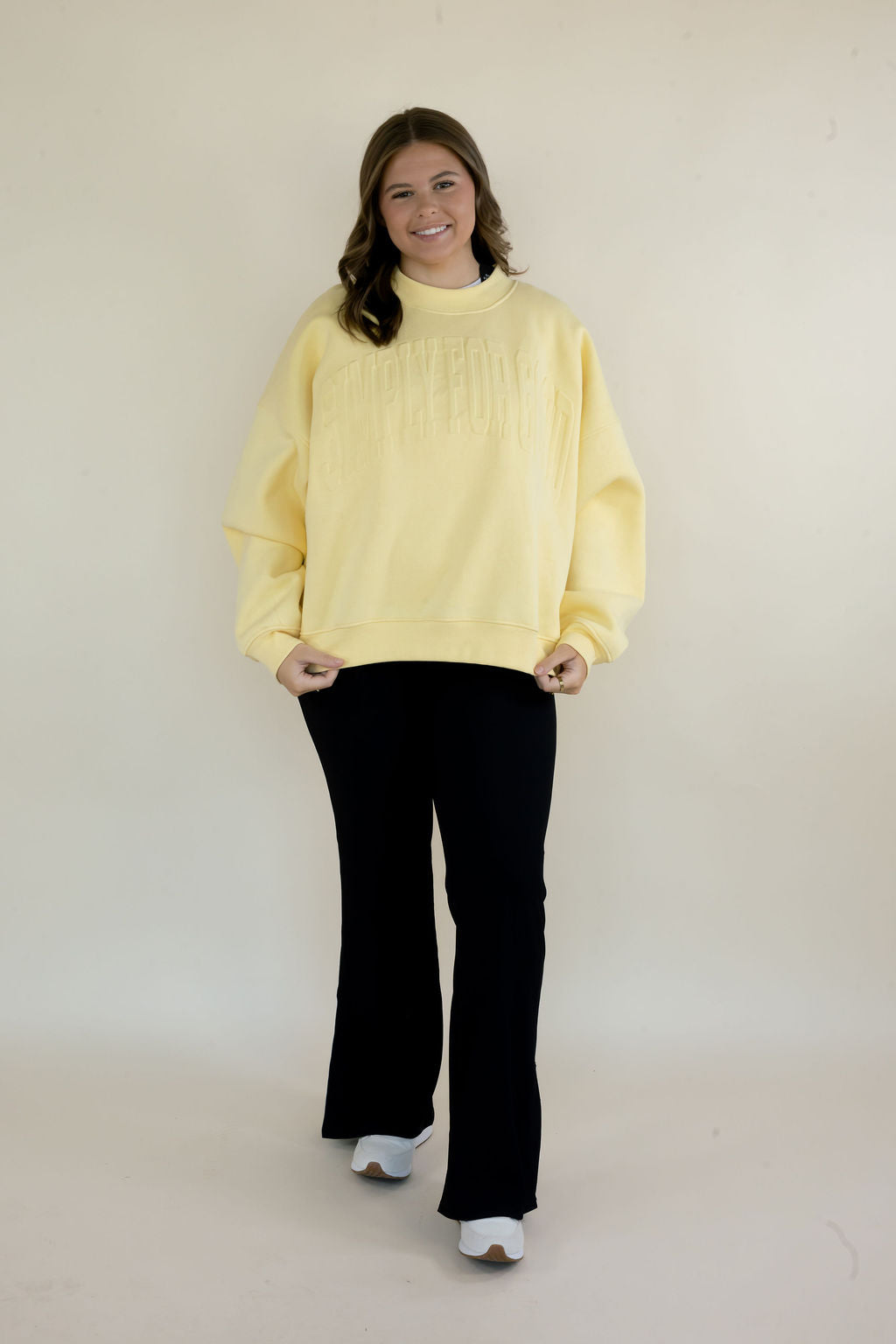 Woman modeling butter yellow Simply For Good crewneck sweatshirt with tonal front lettering and black flare pants