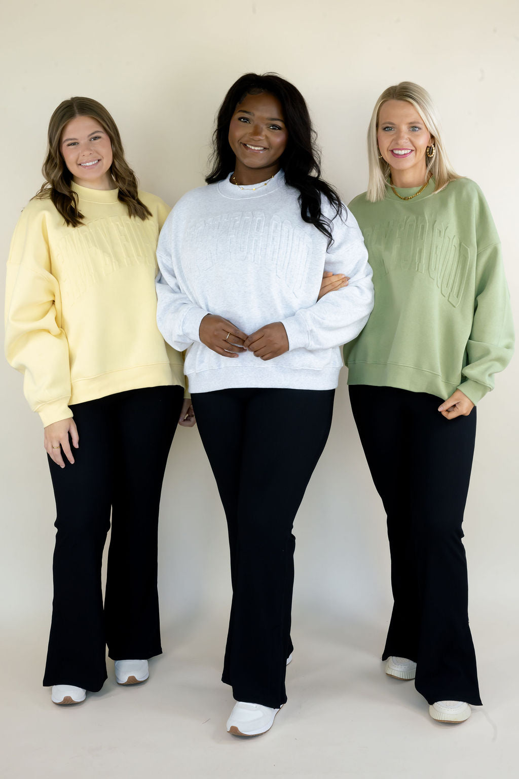 Three women modeling Simply For Good crewneck sweatshirts in butter yellow, heather gray, and sage green with tonal front lettering and black pants
