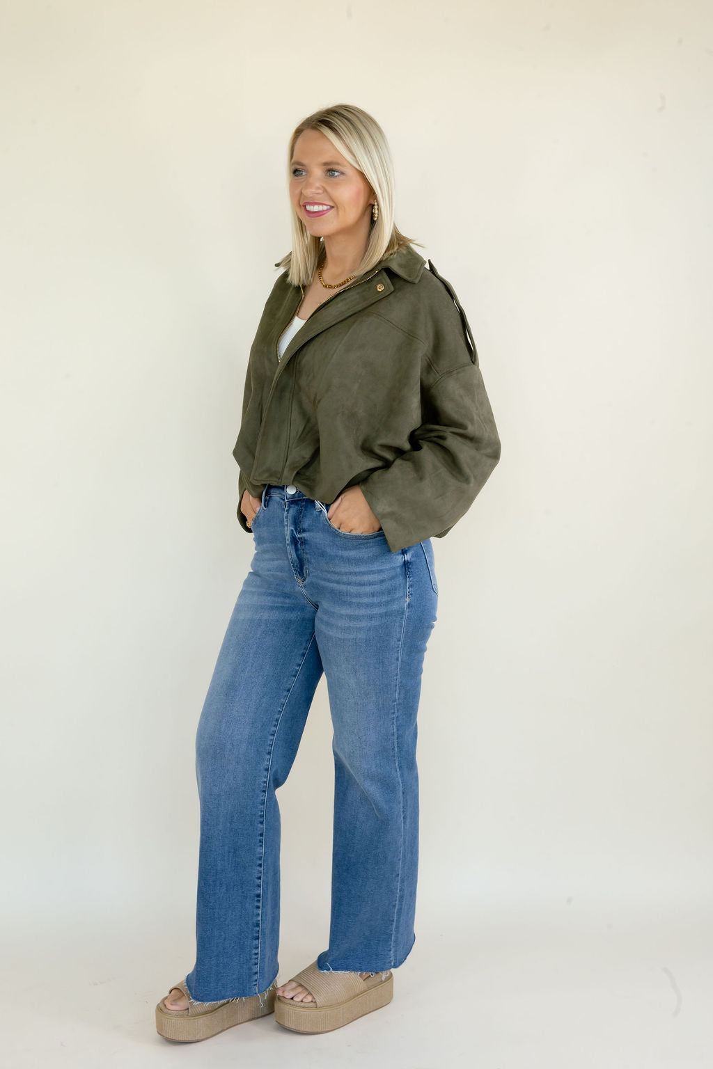 Side view of woman modeling olive green full zip jacket with relaxed silhouette styled with blue straight leg jeans and neutral shoes
