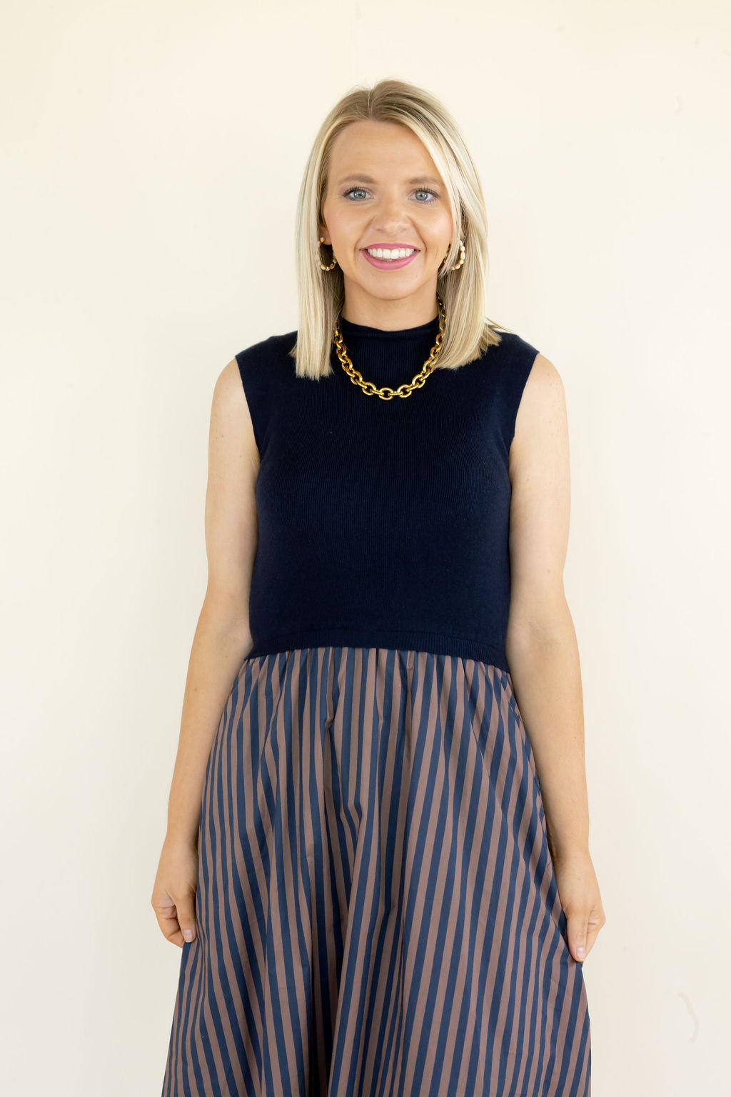 Front view of navy sleeveless midi dress featuring a solid fitted bodice, round neckline, and contrasting striped full skirt