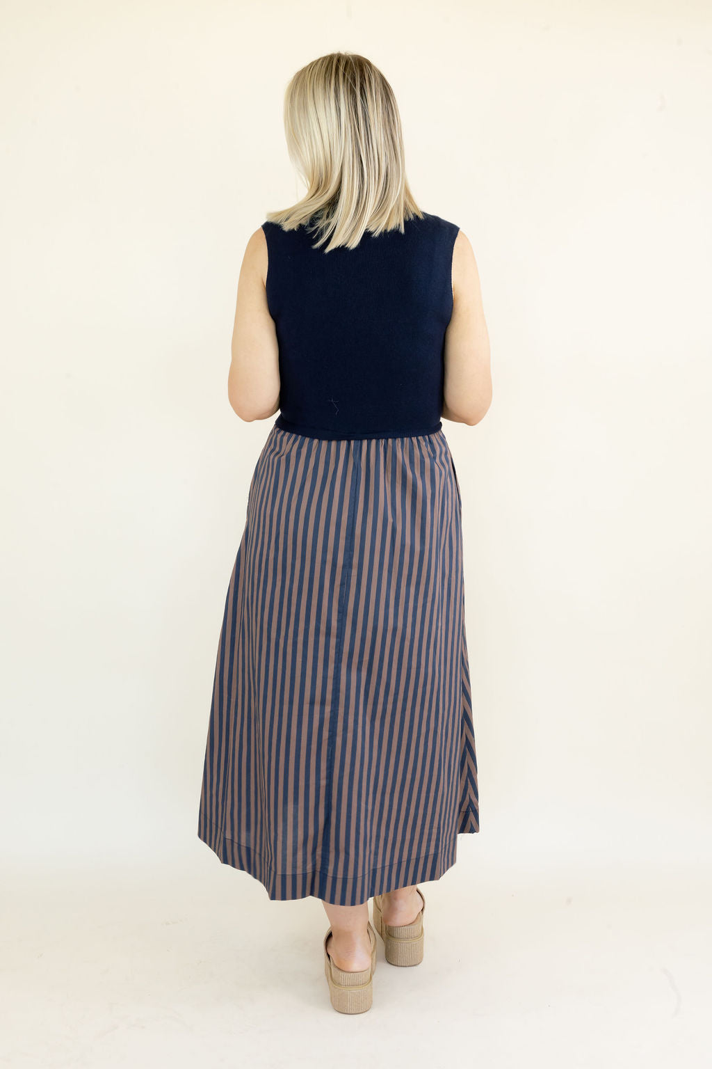 Full back view of navy sleeveless midi dress showing solid navy bodice, gathered striped skirt, and flowy midi-length silhouette
