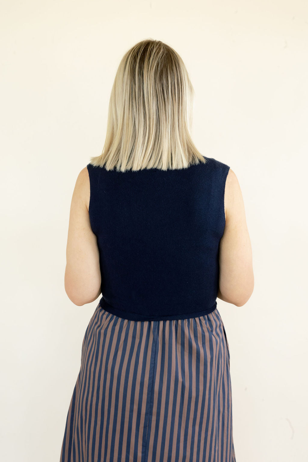 Close back view of navy sleeveless midi dress highlighting the solid knit bodice, sleeveless design, and gathered striped skirt