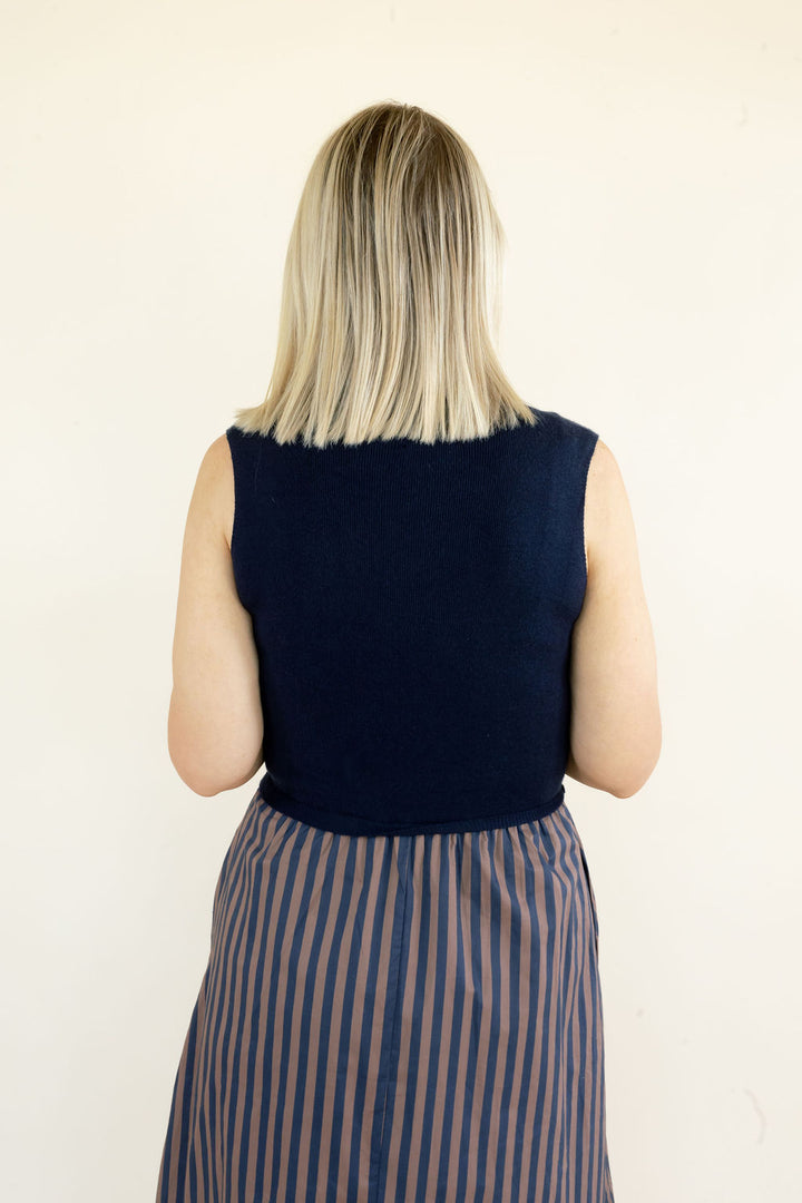 Close back view of navy sleeveless midi dress highlighting the solid knit bodice, sleeveless design, and gathered striped skirt