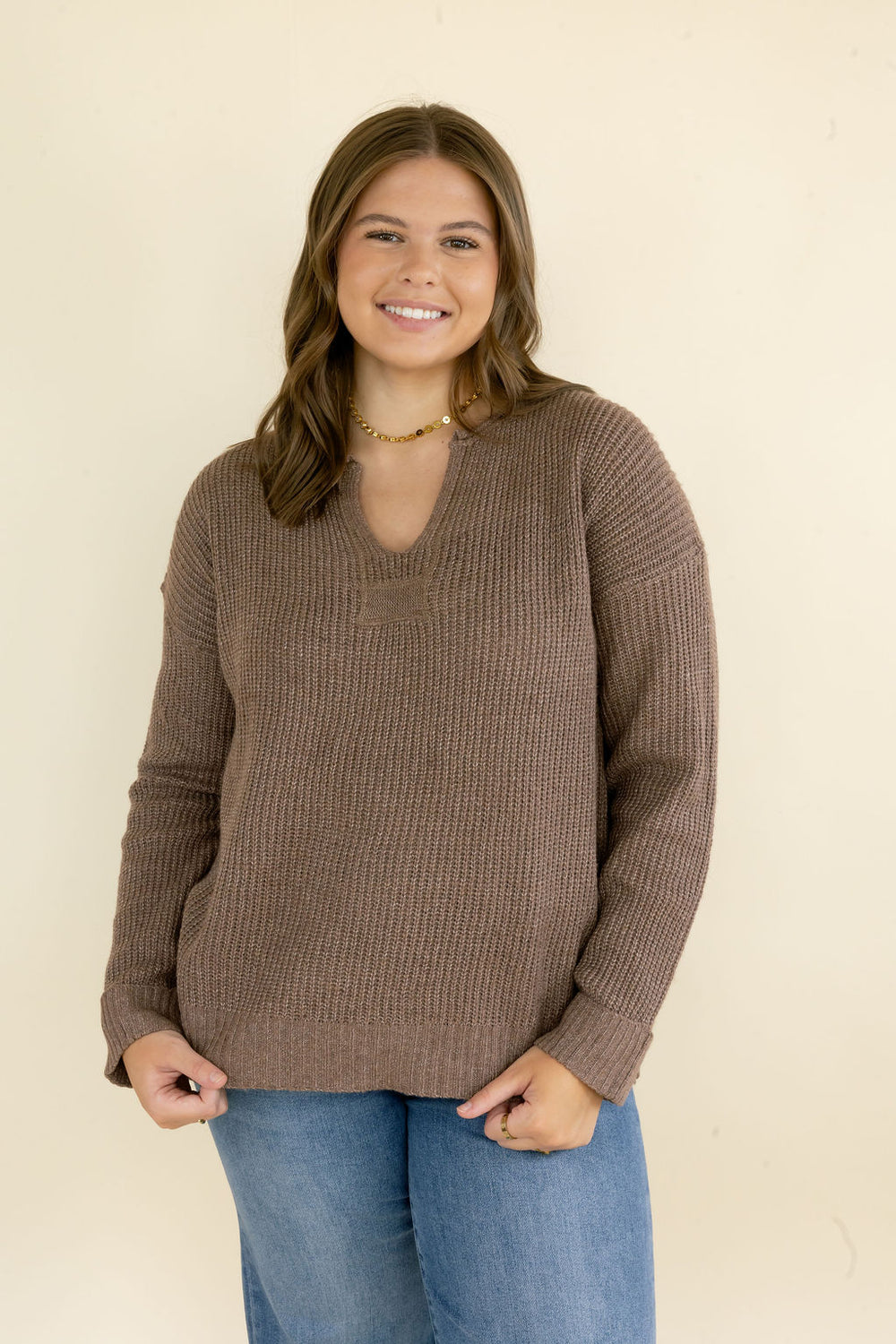 Front view of woman wearing taupe brown V-neck sweater featuring soft knit texture, long sleeves, ribbed trim, and relaxed silhouette