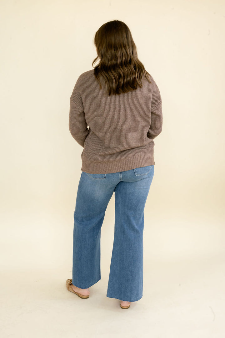 Full back view of woman wearing taupe brown knit sweater with blue wide leg jeans, showing the relaxed silhouette and hip-length hem