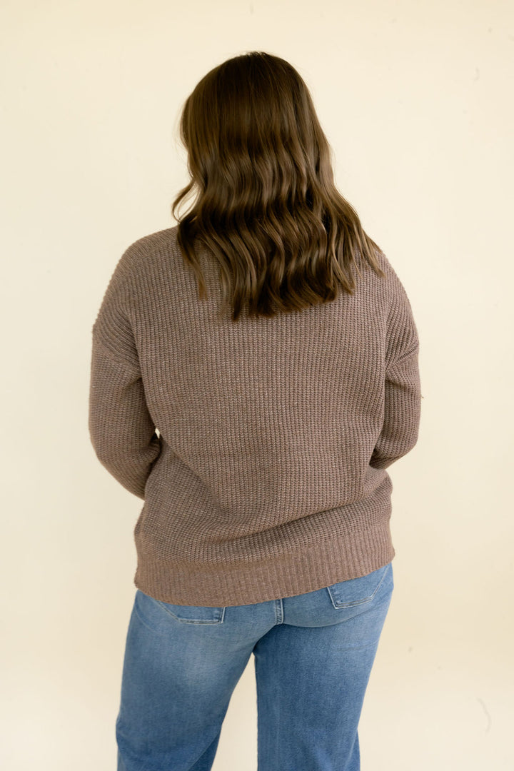 Close back view of taupe brown knit sweater highlighting the textured knit fabric, long sleeves, ribbed hem, and relaxed fit