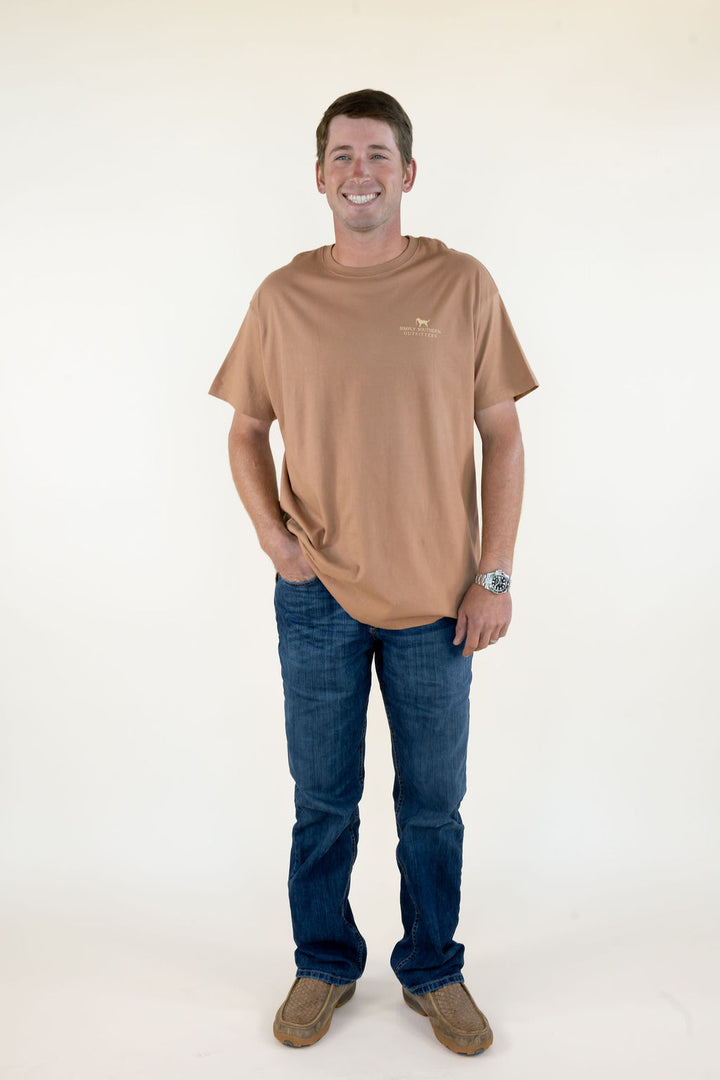 Full-length front view of man wearing tan Marsh &amp; Retrievers short sleeve graphic T-shirt with blue jeans and brown loafers.