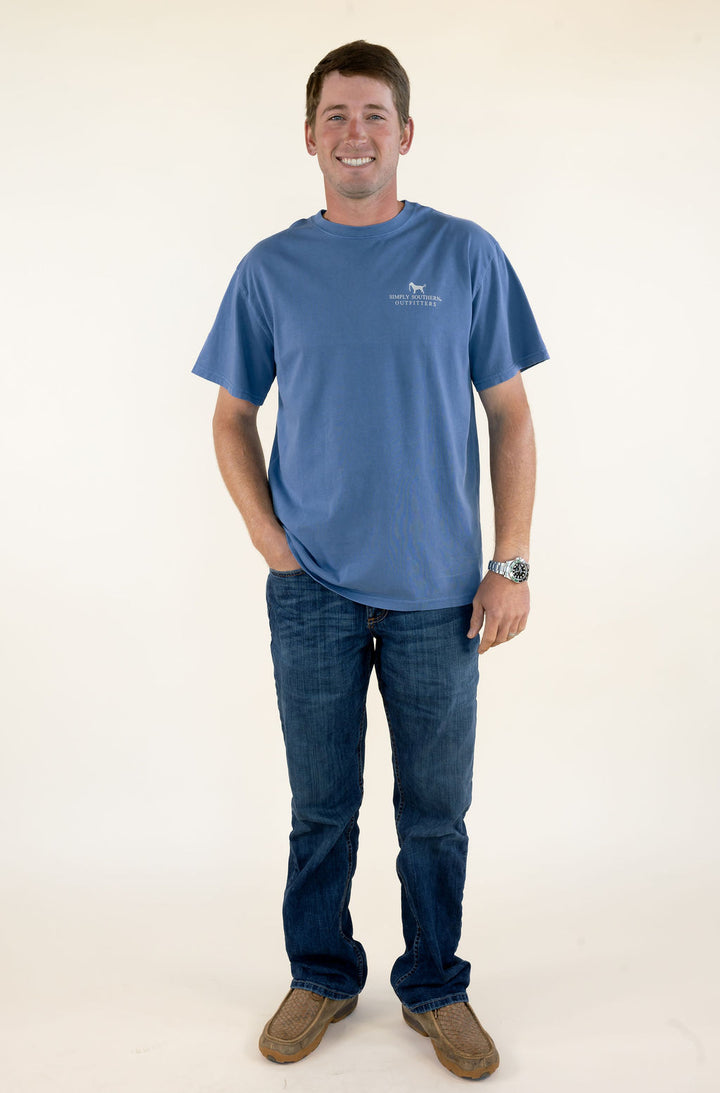 Full-length front view of man wearing blue Simply Southern short sleeve graphic T-shirt with jeans and brown boots