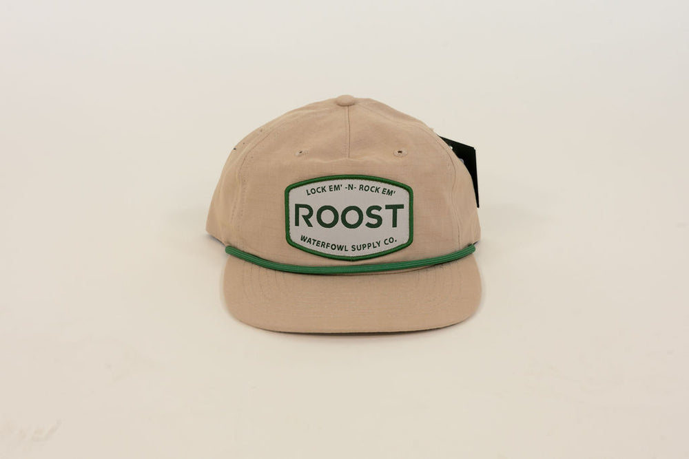 Close-up of tan Roost Waterfowl Supply Co. cap featuring green embroidered logo patch, green rope detail, and flat bill