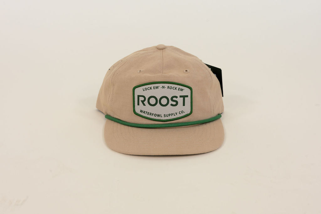Close-up of tan Roost Waterfowl Supply Co. cap featuring green embroidered logo patch, green rope detail, and flat bill