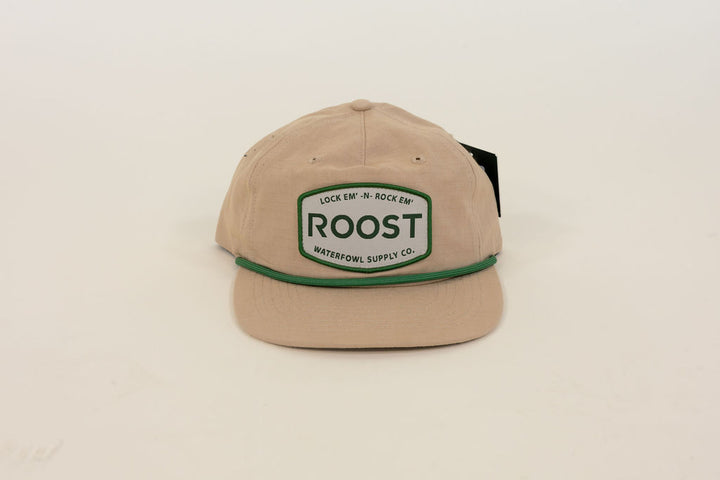 Close-up of tan Roost Waterfowl Supply Co. cap featuring green embroidered logo patch, green rope detail, and flat bill
