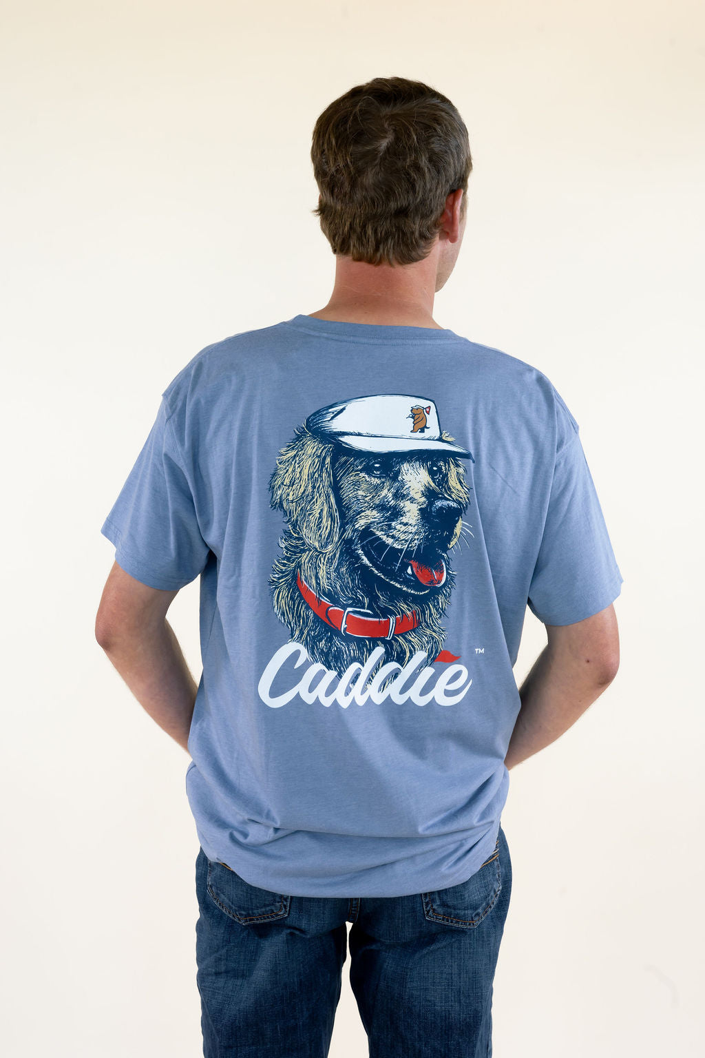 Man modeling blue Caddie graphic T-shirt featuring a large golf dog back graphic with white Caddie lettering, short sleeves, and relaxed fit