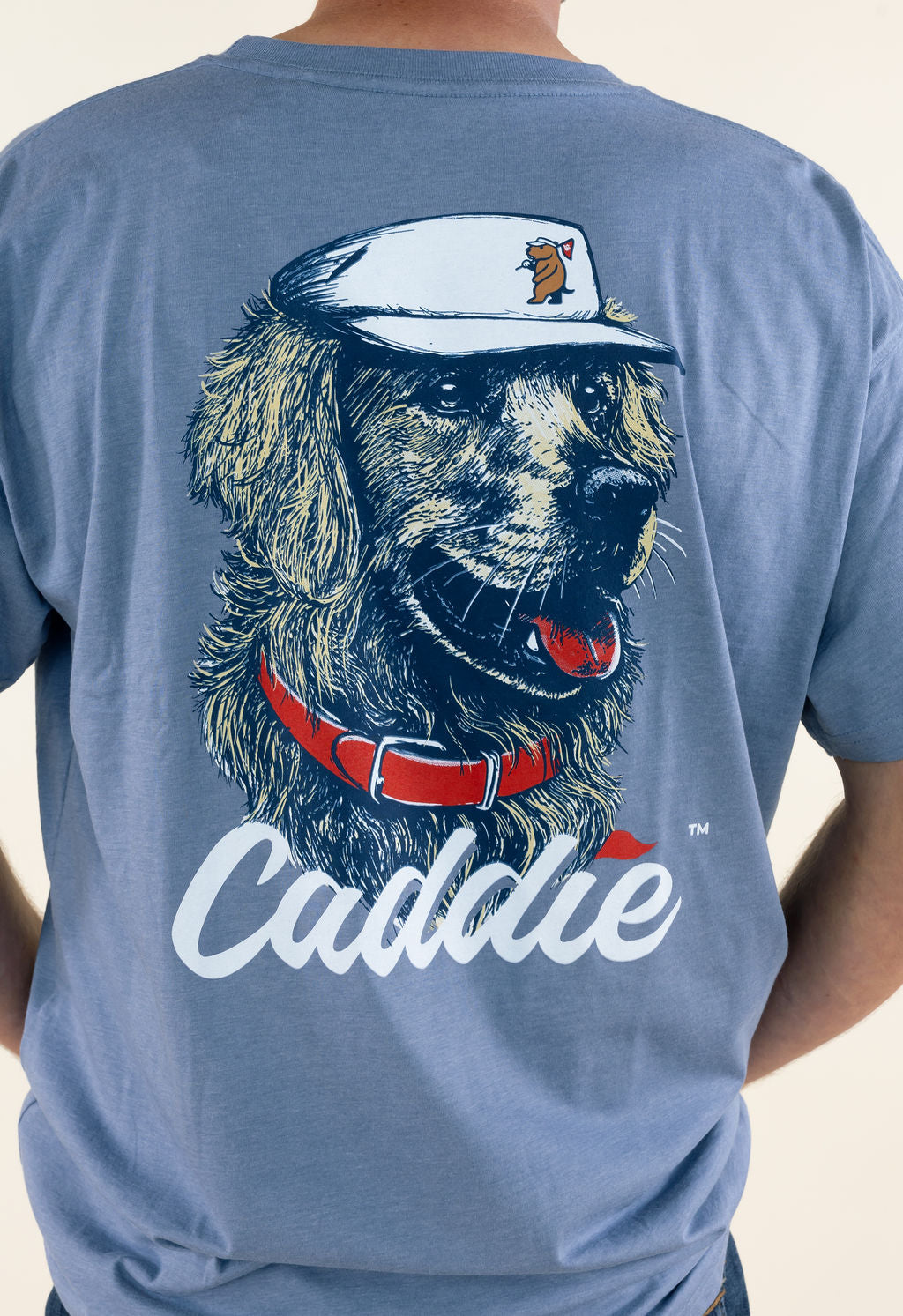 Close-up back view of blue Caddie graphic T-shirt highlighting the large golf dog wearing a visor with golf-inspired details and white Caddie lettering