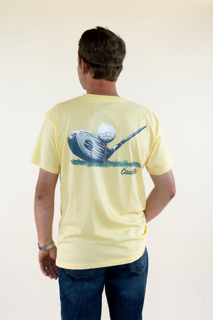Man modeling pale yellow Caddie golf graphic T-shirt featuring a large golf ball, club, and cup back graphic with short sleeves and relaxed fit
