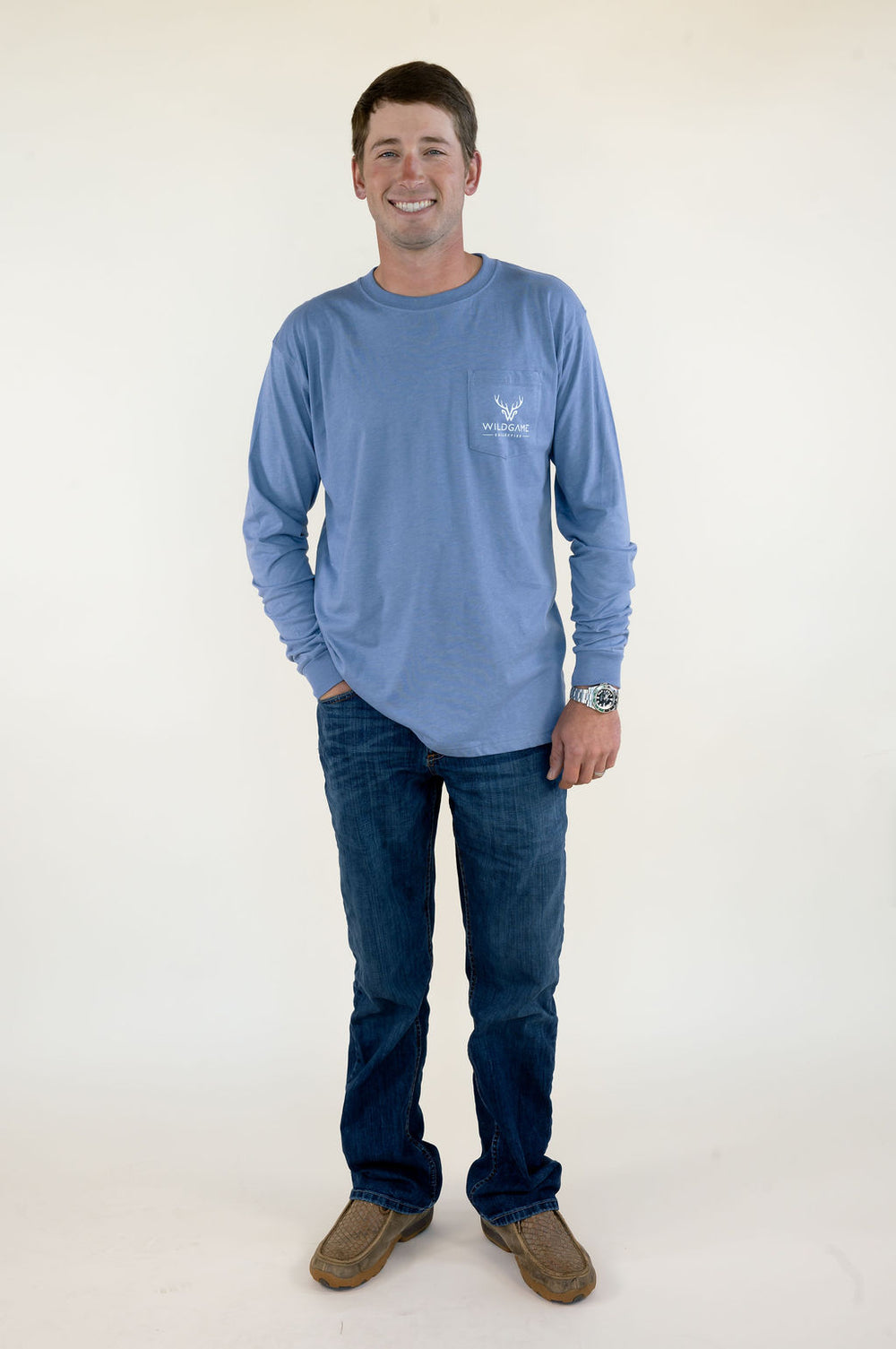 Full-length front view of man wearing blue Wildgame long sleeve graphic shirt with blue jeans