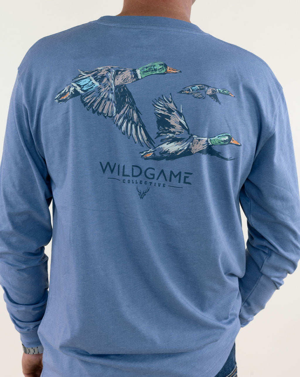 Close-up back view of blue Wildgame long sleeve graphic shirt highlighting flying mallard ducks with camouflage detailing and Wildgame lettering