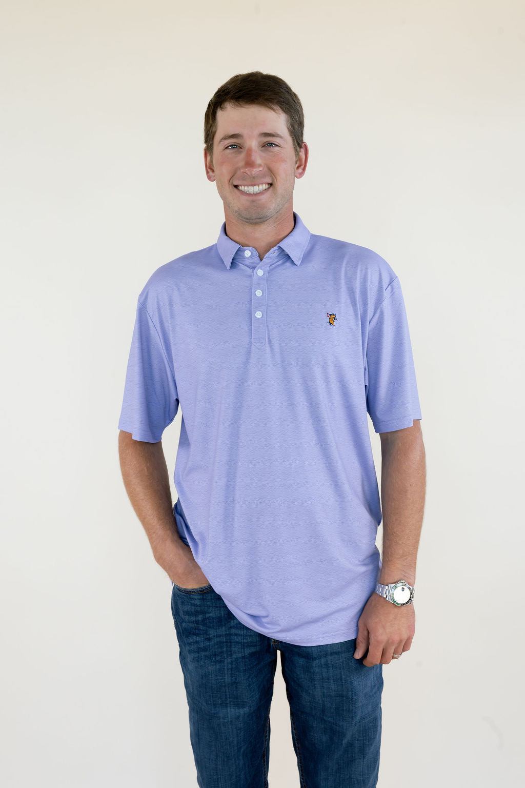 Front view of man wearing light lavender men’s performance polo featuring short sleeves, button placket, relaxed fit, and small embroidered chest logo
