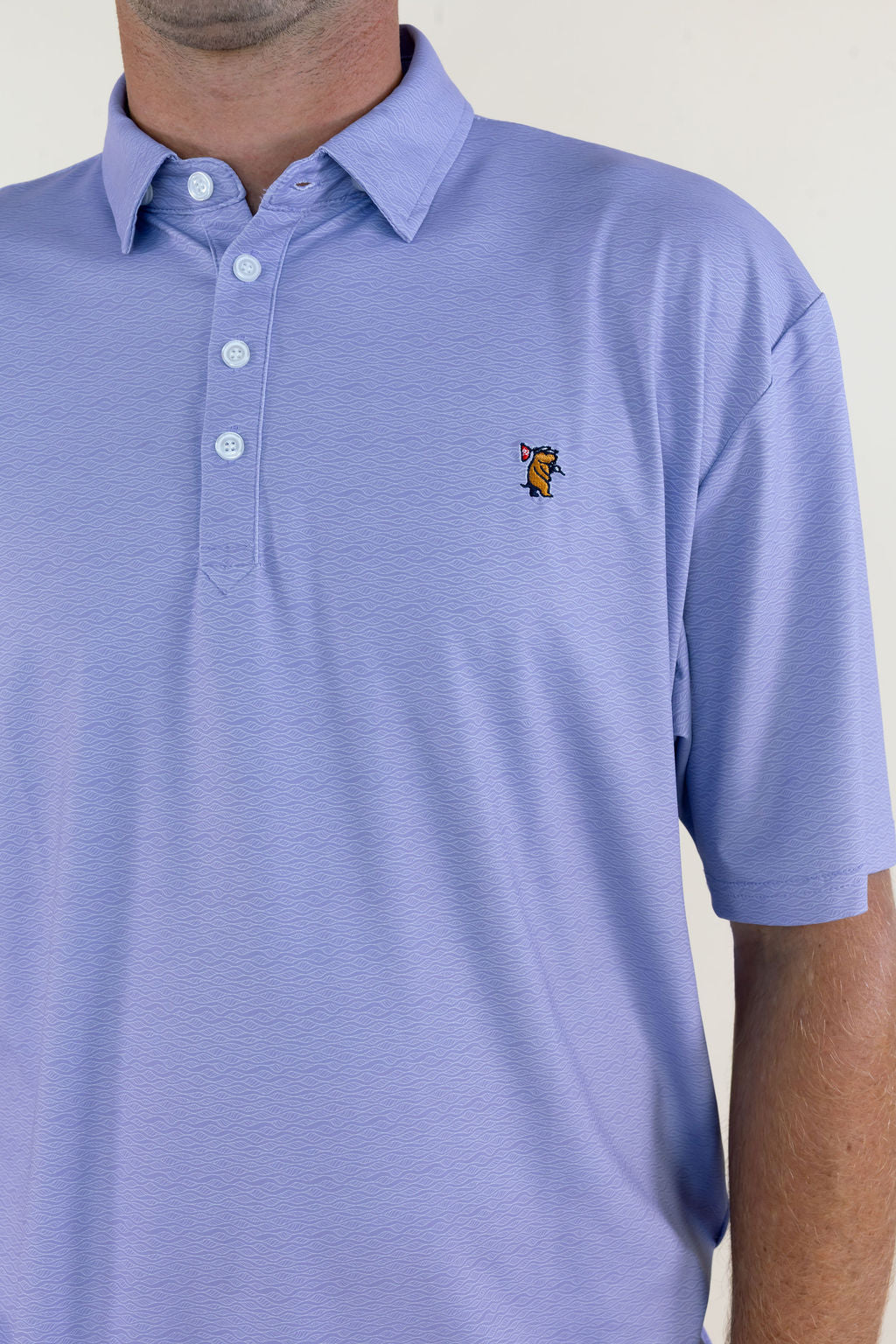 Close-up of light lavender men’s polo highlighting the collared neckline, three-button placket, smooth performance fabric, and small embroidered chest logo