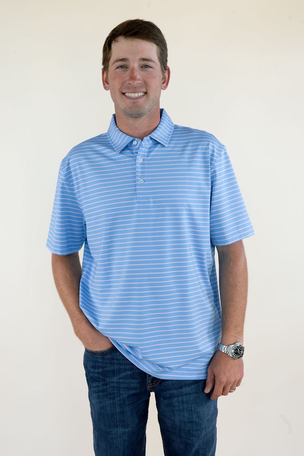 Front view of blue and pink striped men’s performance polo featuring short sleeves, collared neckline, button placket, and relaxed fit
