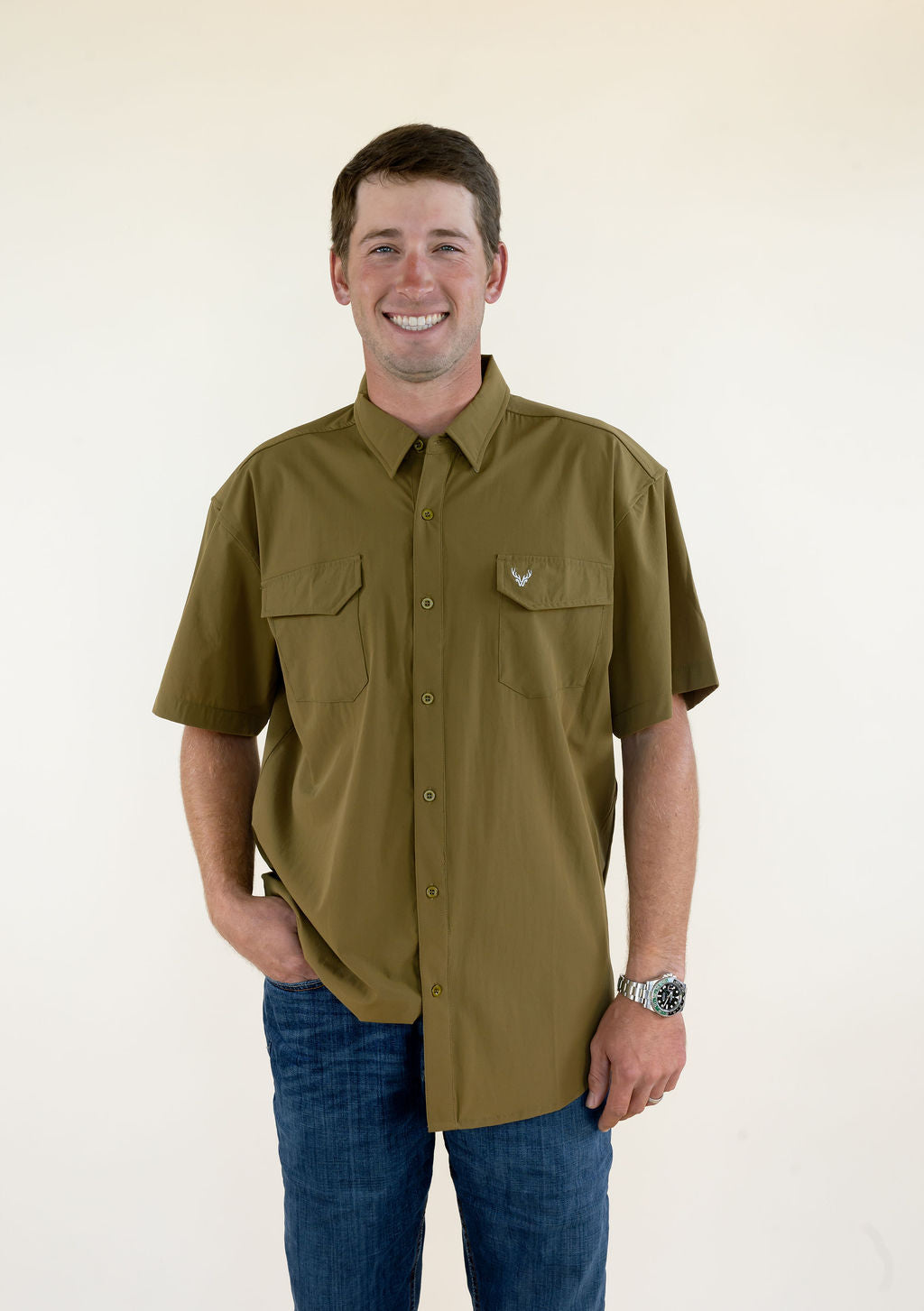 Front view of male model wearing the olive WILDGAME Maverick short sleeve button down performance shirt with chest pockets.