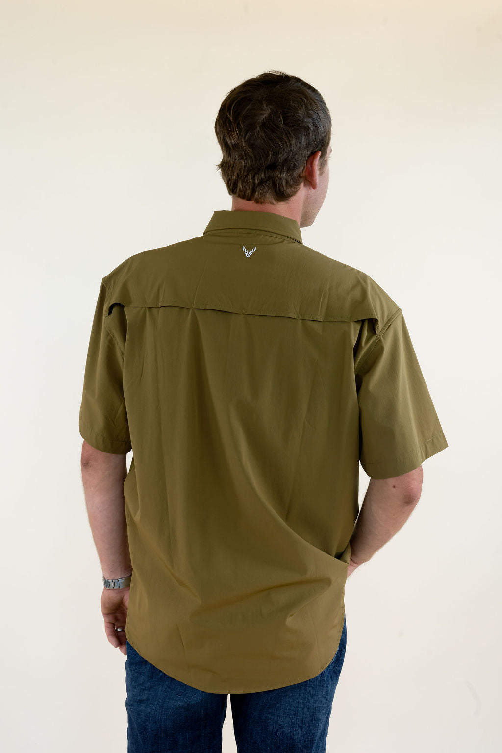 Back view of male model wearing the WILDGAME Maverick olive short sleeve performance button down shirt showing the vented back design.
