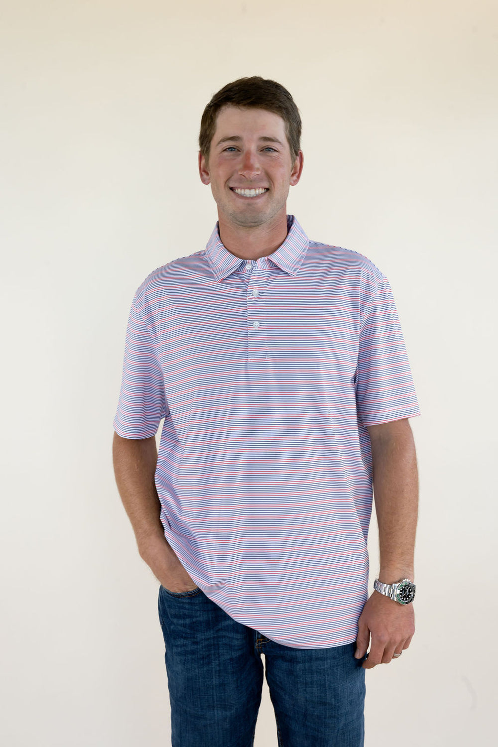 Male model wearing a cream striped short sleeve performance polo shirt with a collared neckline, front view. with blue jeans, full-body front view.