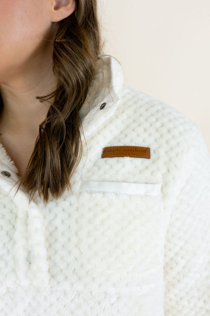 Close-up of ivory Simply Southern Simply Soft Pullover showing plush textured fabric, snap-button collar, chest pocket, and Simply Southern leather logo patch.