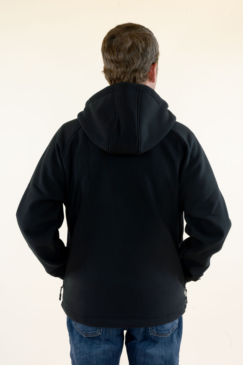 Back view of male model wearing the black Roost Defender Pullover showing the attached hood and soft shell construction.