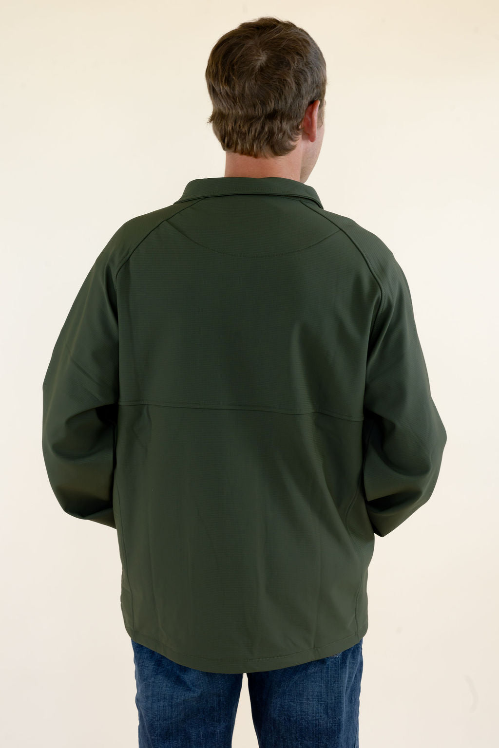 Back view of male model wearing the green Dogwood Pullover showing the solid green soft shell construction and rear fit.