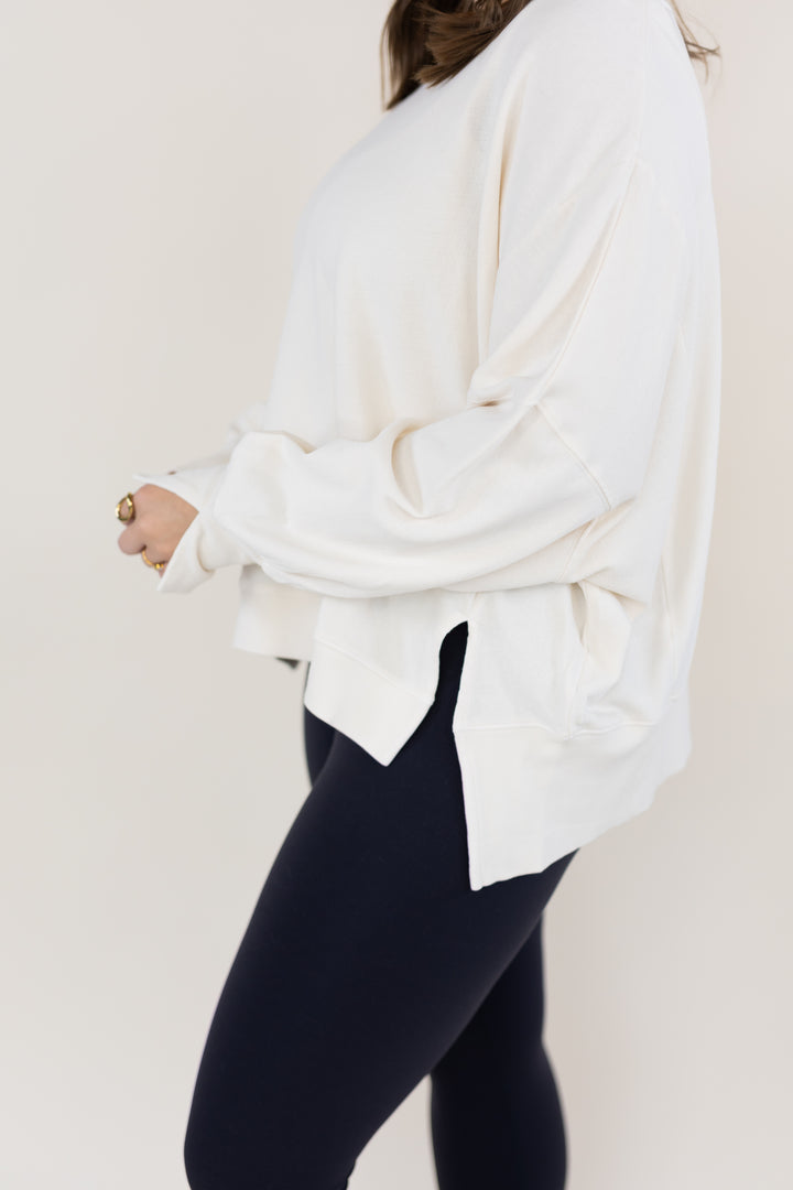 A person wearing an oversized off-white long-sleeve top and black leggings, shown from the side against a plain light beige background.