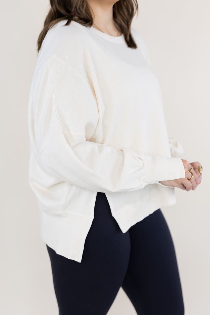 A woman wearing a loose white long-sleeve crewneck sweatshirt and dark navy leggings, shown from the shoulders down against a plain light beige background.