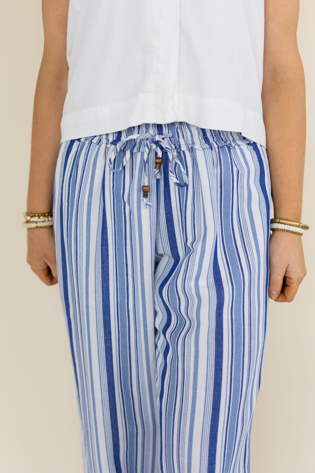 A person wearing loose blue and white vertically striped drawstring pants with a white sleeveless top, shown from the chest down against a plain light beige background.