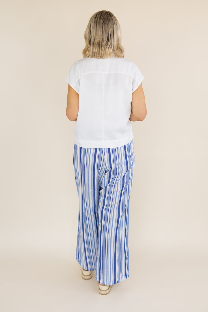 A woman viewed from behind wearing a white short-sleeve top and blue-and-white vertically striped wide-leg pants, standing against a plain beige studio background.