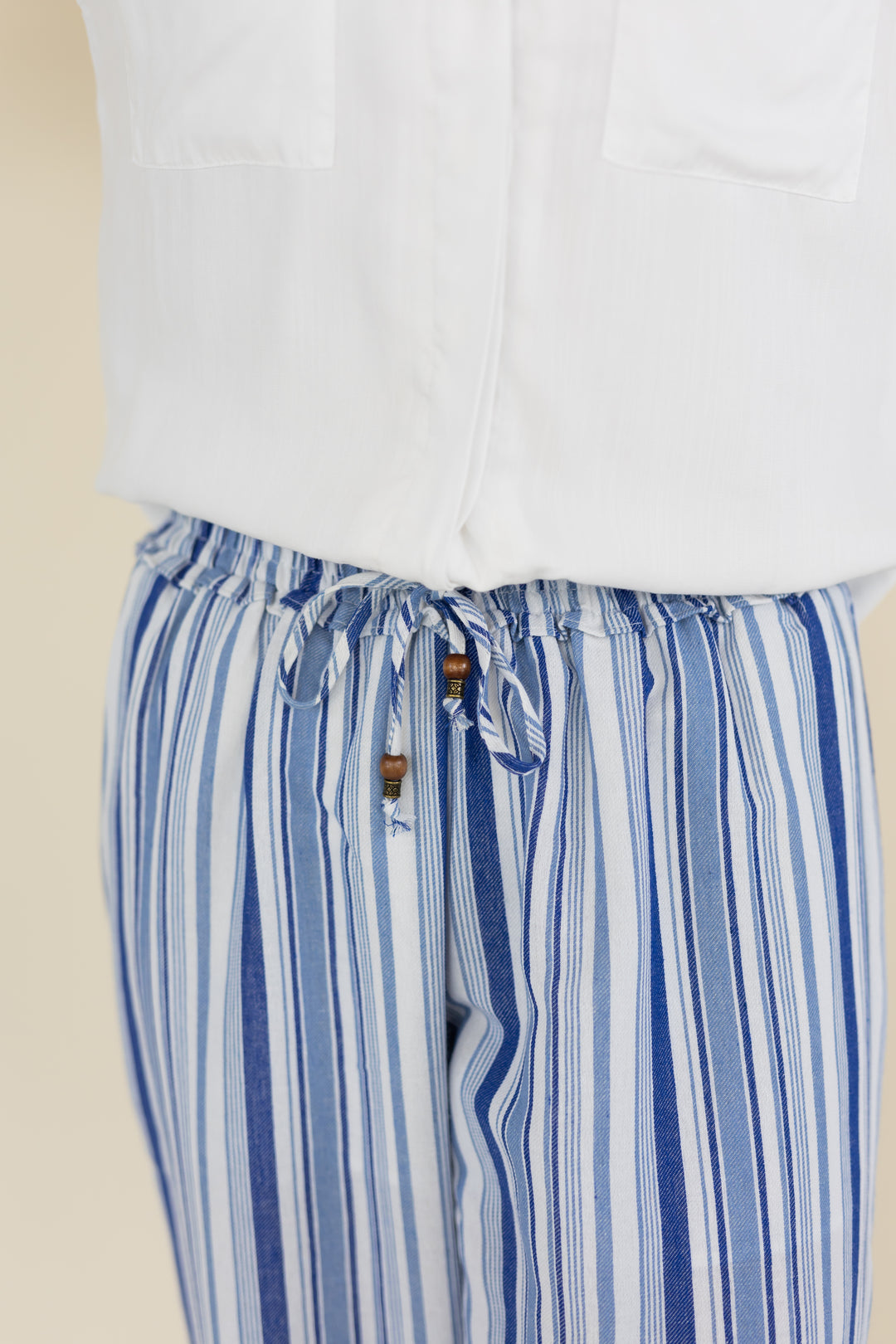 Close-up of a person wearing blue and white vertically striped drawstring pants with a white top, against a plain light beige background.