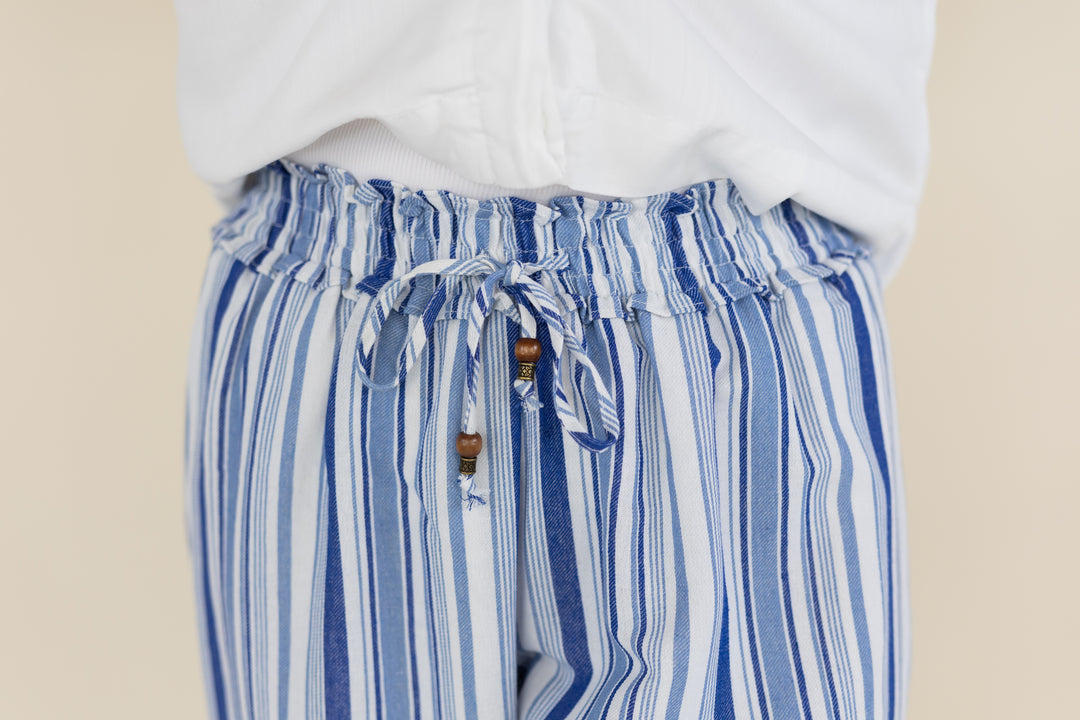 Close-up of a person wearing blue and white vertically striped drawstring pants with a white top, against a plain beige background.