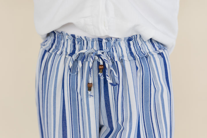 Close-up of a person wearing blue and white vertically striped drawstring pants with a white top, against a plain beige background.