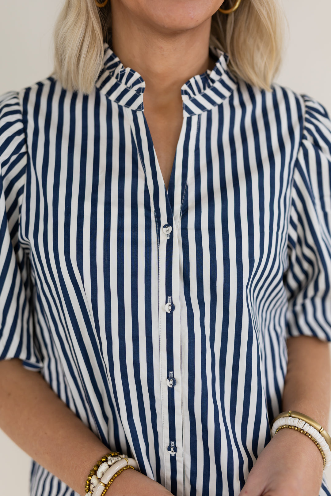 A close-up of a woman wearing a navy and white vertically striped short-sleeve button-up shirt with a ruffled collar.