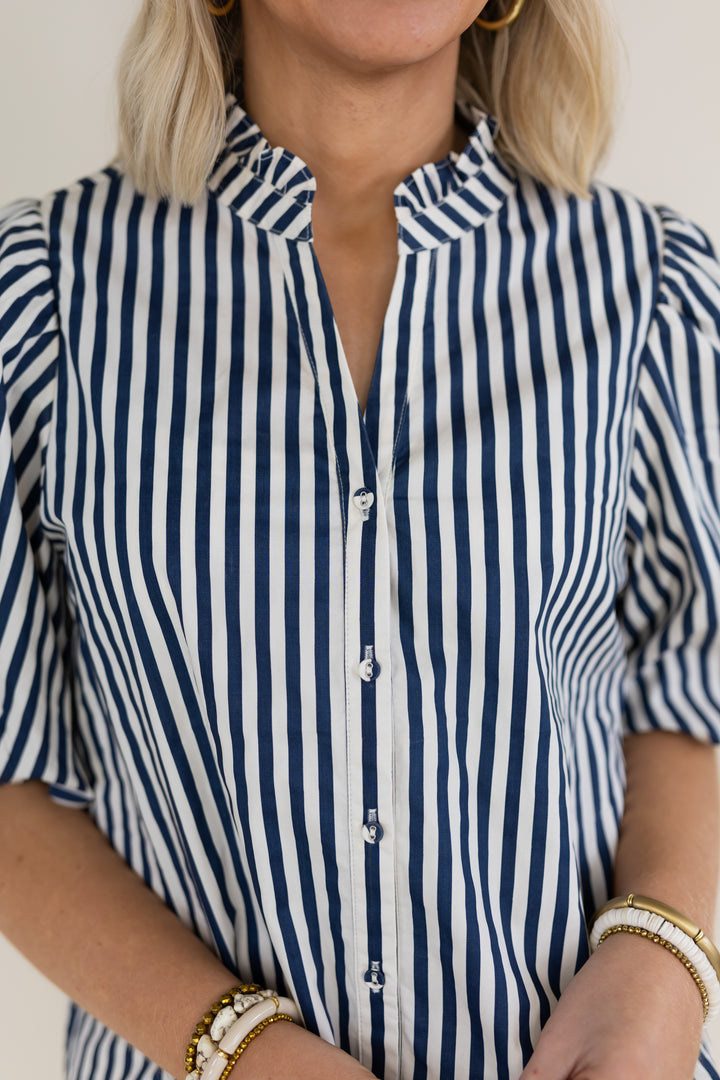 A close-up of a woman wearing a navy and white vertically striped short-sleeve button-up shirt with a ruffled collar.