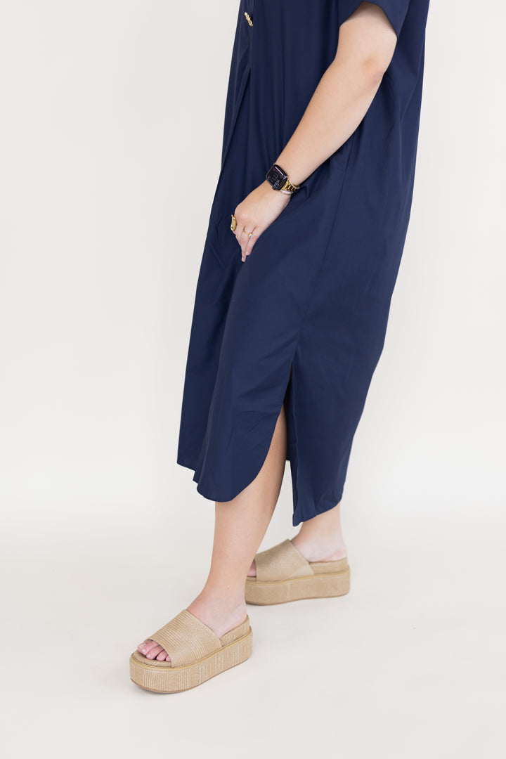 A person wearing a loose navy midi dress with a side slit, paired with beige platform slide sandals and a black watch, shown against a plain light background.