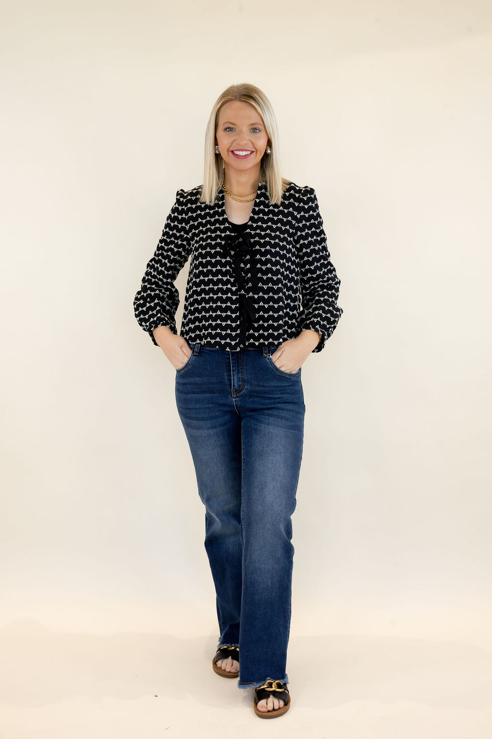 Full-length view of woman wearing black and white textured sweater jacket with front bow details, cropped silhouette, and blue wide leg jeans