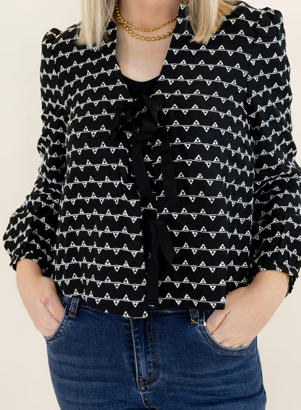 Close-up of black and white patterned sweater jacket highlighting the decorative black bow closures, textured knit fabric, round neckline, and long sleeves