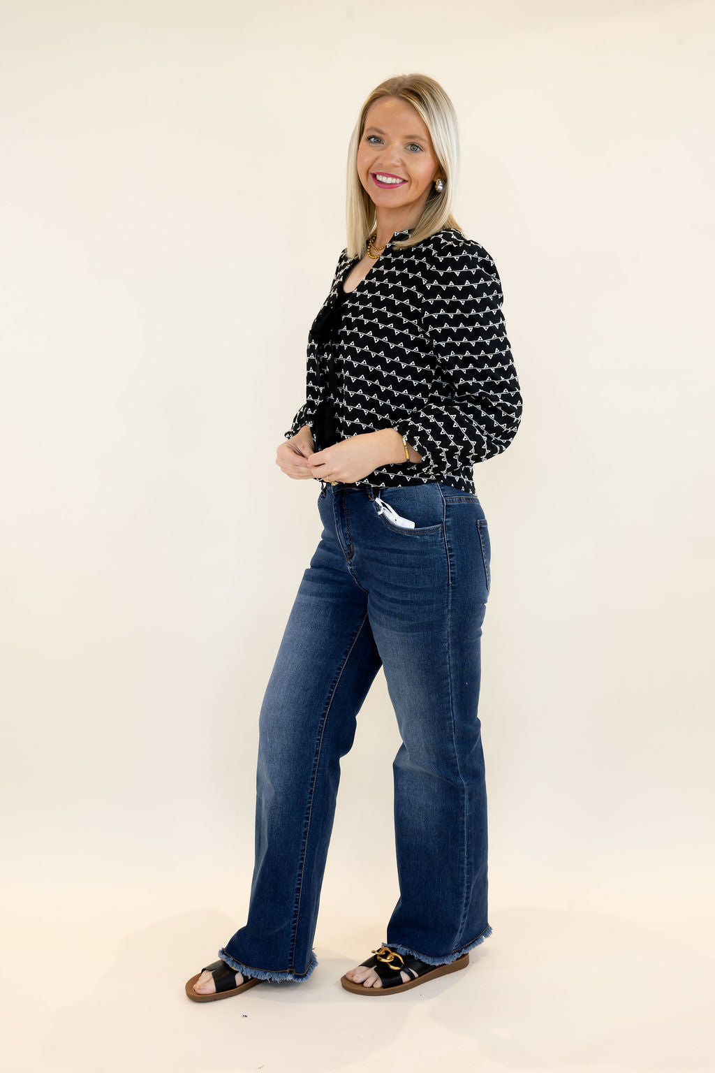Side view of woman modeling black and white cropped sweater jacket with textured pattern, relaxed fit, and blue wide leg jeans