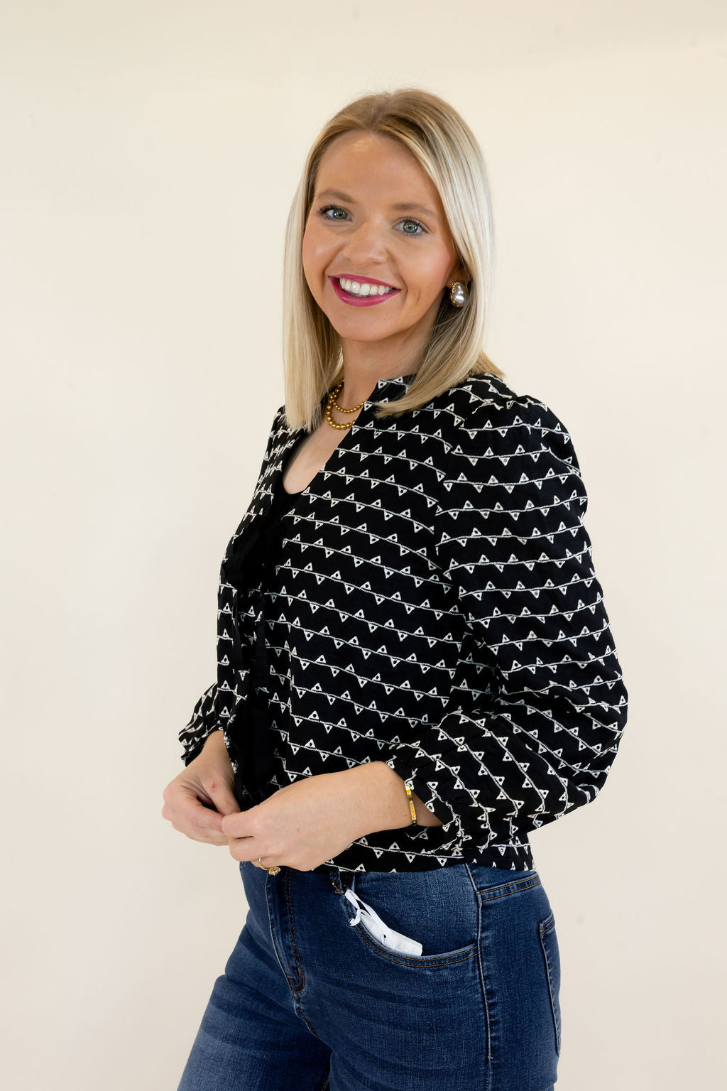 Three-quarter view of black and white patterned sweater jacket featuring black bow tie closures, structured shoulders, and cropped length