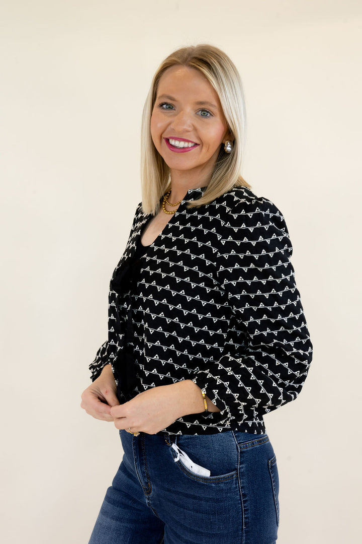 Three-quarter view of black and white patterned sweater jacket featuring black bow tie closures, structured shoulders, and cropped length