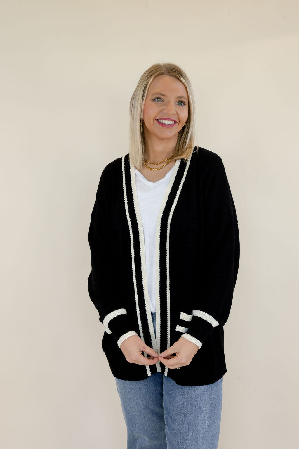 Front view of black open-front knit cardigan featuring white trim along the neckline and front opening, relaxed silhouette, and contrasting pocket details