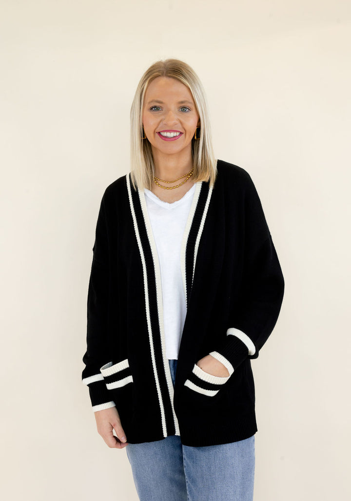 Three-quarter view of woman modeling black and white contrast trim cardigan with relaxed fit, front pockets, and light wash denim jeans