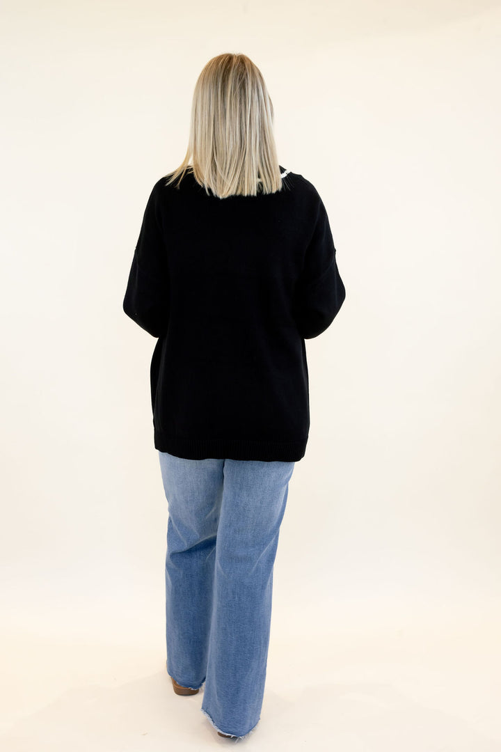 Full back view of woman wearing black knit cardigan with relaxed fit, long sleeves, and straight hem styled with light wash wide leg jeans