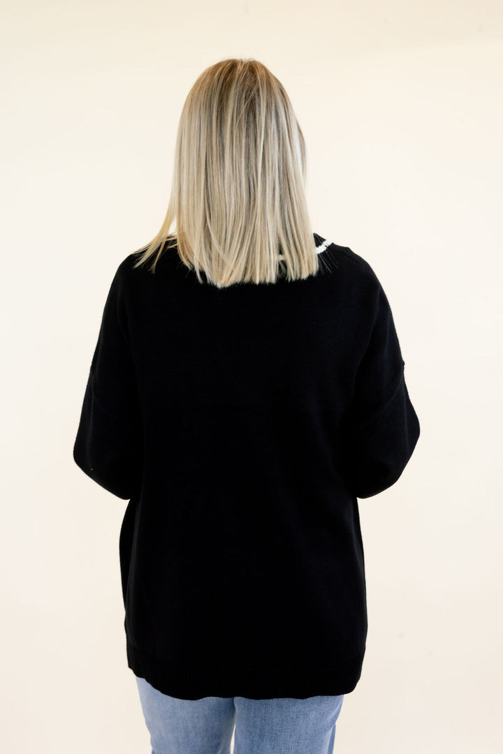 Back view of black knit cardigan showing the solid black design, relaxed silhouette, long sleeves, and hip-length hem